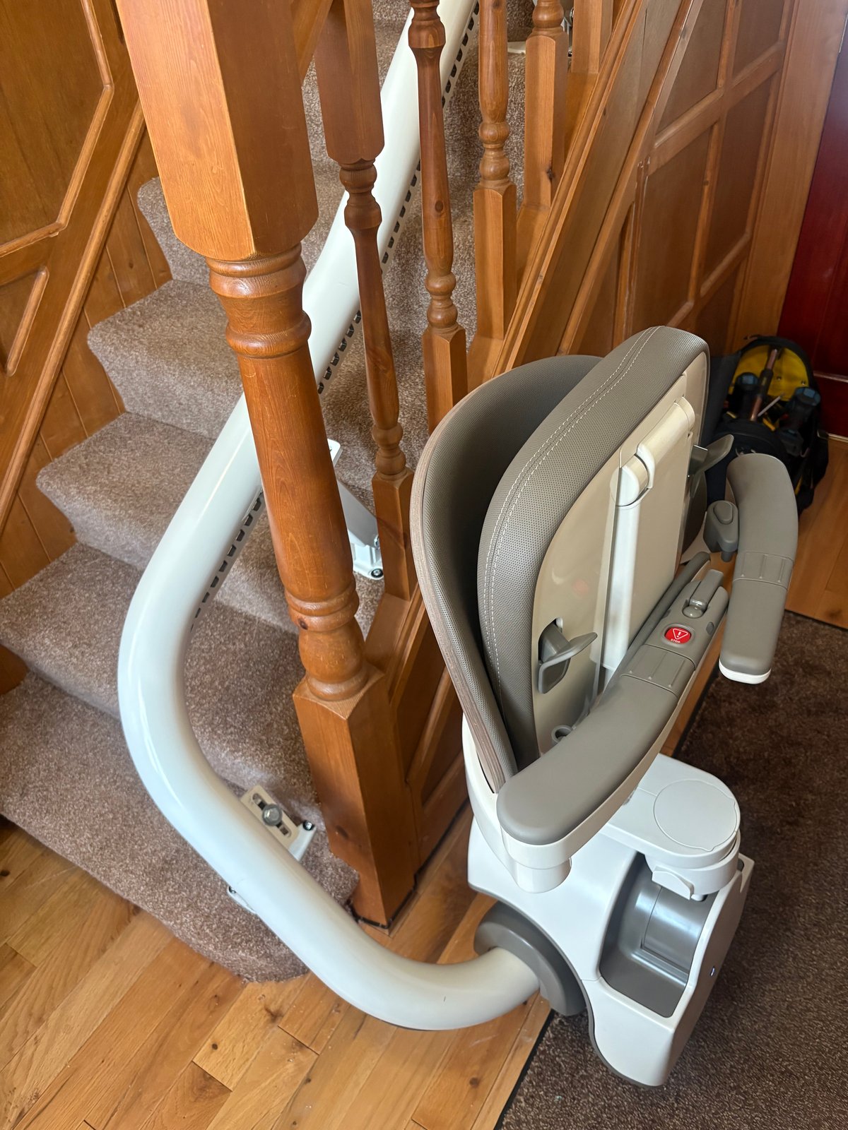 Curved stairlift with a folded grey seat and a white rail wrapping around the bottom of a wooden staircase