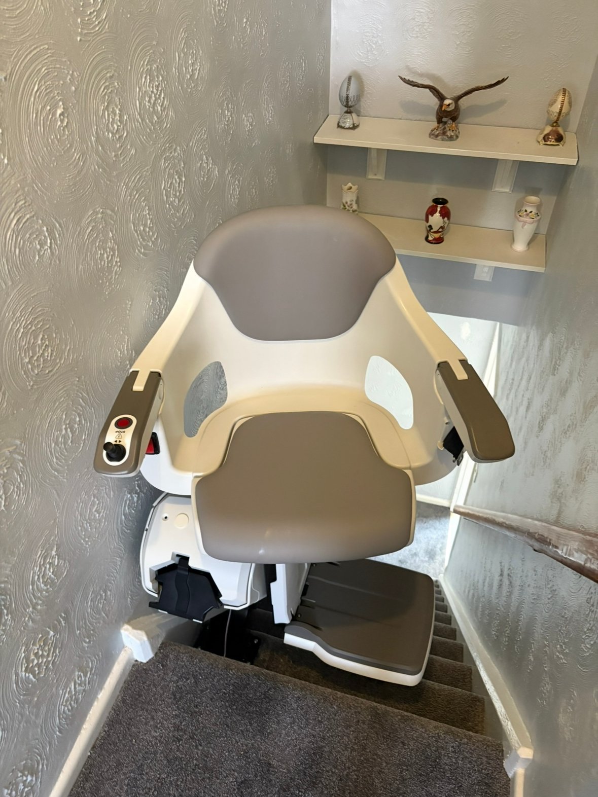 Straight stairlift at the top of carpeted stairs, with its grey seat swivelled towards the landing